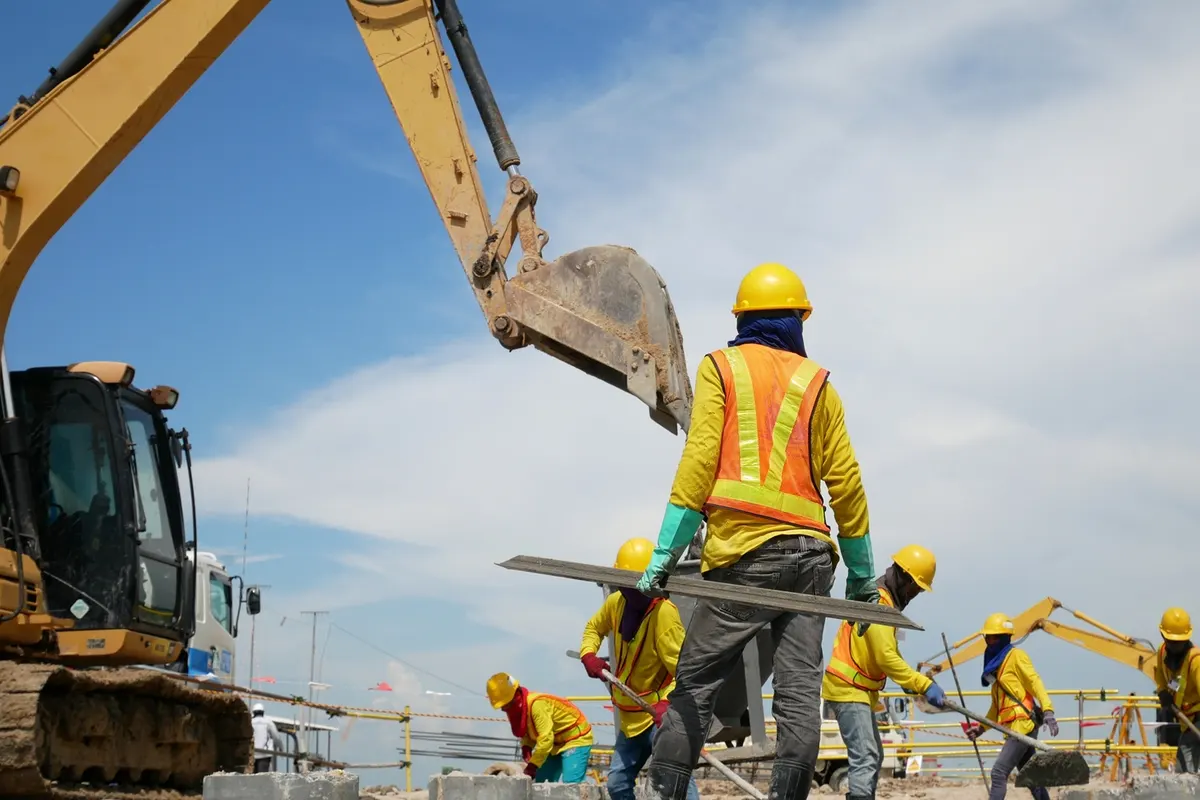Operarios con casco y chaleco trabajando junto a una excavadora en una obra